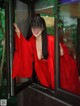 A woman in a red robe is looking out of a window.