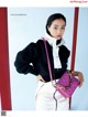 A woman in a black sweater and white pants holding a purple purse.