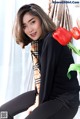 A woman sitting on a stool next to a vase of flowers.