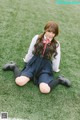 A woman in a school uniform sitting on the grass.