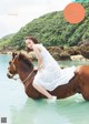 A woman in a white dress riding a brown horse in the water.