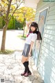 A woman in a school uniform leaning against a wall.