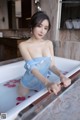 A woman in a blue dress sitting in a bathtub.