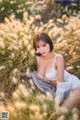 A woman in a white lingerie sitting in tall grass.