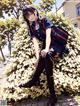 A girl in a school uniform sitting on a bush.